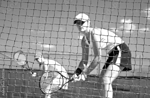 Photo: woman tennis players looking at camera through net waiting to pl woman tennis players looking at camera through net waiting to pl