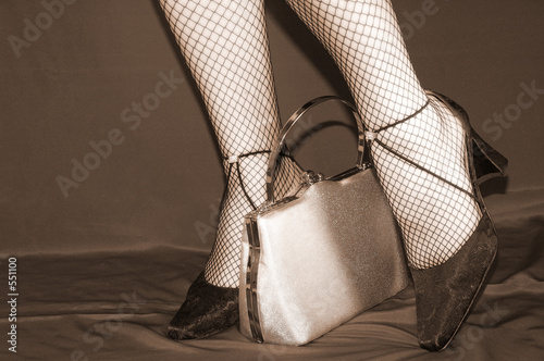 legs of a woman with black shoes on and shiny silver purse