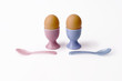 two brown eggs in cups with spoons on white backgr