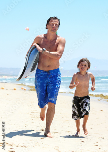 Photo: young father and son running along beach with surfboard young father and son running along beach with surfboard