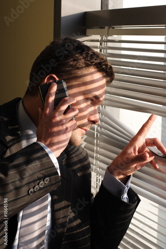 business man on phone  looking through window blin
