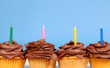 four chocolate frosted cupcakes in a row with candles