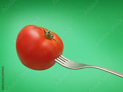 fresh tomato on fork with green background