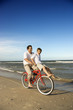 Dad riding red bicycle with son on handlebars.