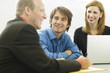 three workers sit and talk at a desk three workers sit and talk at a desk