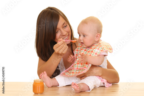 mother and 8 months baby girl with baby food isolated on white mother and 8 months baby girl with baby food isolated on white