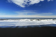 waves crashing on a sandy black beach , deep blue sky