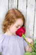 a little girl smelling a big red rose