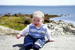 Cute baby in sunshine sitting on a rock by the sea