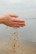 falling sand in female hands over sea