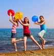 Three girls with colorful beach balls walking on sea shore