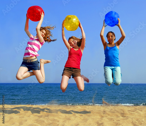 Foto: Three girls with colorful beach balls jumping on a seashore Three girls with colorful beach balls jumping on a seashore