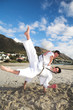 Young adult men with black belt practicing karate on the beach 