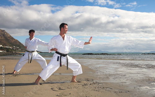Photo: Young adult men with black belt practicing a Kata on the beach Young adult men with black belt practicing a Kata on the beach