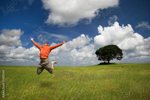 Man jumping on a green meadow with a beautiful cloudy sky
