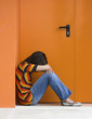 Loneliness woman on a orange door with hands over the knees
