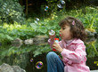 Little girl at the park pond blowing soap bubbles