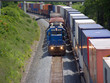 Locomotive pulling short train beside parked container cars
