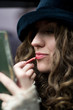 young model in hat retouching the lips with red pencil