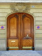Porte cochère marron, poignées dorées, façade de pierre
