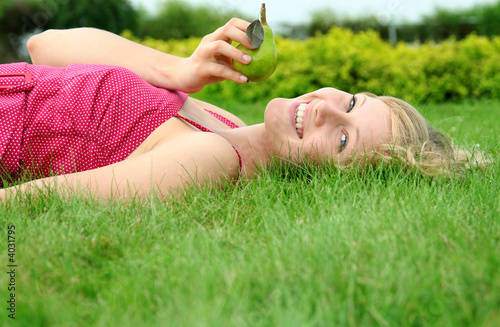 Photo: Young woman lying on a lawn holding a pear Young woman lying on a lawn holding a pear