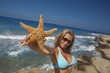 Young woman holding a starfish in front of the ocean