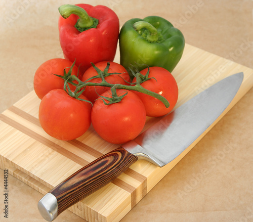 Tomatoes and peppers on chopping board with large knife