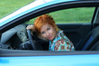 Young red-haired woman is siting in a car. Woman is happy