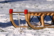 Schlitten steht im Schnee, Rasen scheint durch