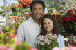 Couple holding plants in plant nursery, portrait