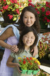 Mother with daughter holding young flowers in plant nursery, portrait