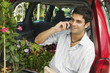 Man sitting by flowers on back of minivan using cell phone