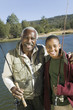 Grandfather and grandson holding fishing rods by lake, smiling, portrait