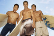 Three surfers standing with surfboards, making faces, outdoors, low angle view
