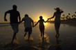 Family running through sea holding hands at sunset, back view, silhouette