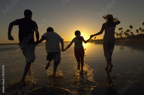 Photo: Family running through sea holding hands at sunset, back view, silhouette Family running through sea holding hands at sunset, back view, silhouette