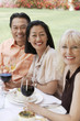 Photo: Three people smiling while sitting at outdoor table holding wine glasses Three people smiling while sitting at outdoor table holding wine glasses