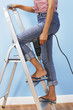 Foto: Woman holding power drill on stepladder, low section Woman holding power drill on stepladder, low section