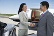 Photo: Business People standing near sports car and private airplane, Shaking Hands, side view Business People standing near sports car and private airplane, Shaking Hands, side view