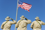 Photo: Rear view of three U.S military personnel saluting the American flag against bright blue sky Rear view of three U.S military personnel saluting the American flag against bright blue sky