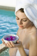 Woman wearing robe holding bowl of orchids next to pool.
