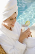 Photo: Woman wearing robe and towel drinking next to pool. Woman wearing robe and towel drinking next to pool.