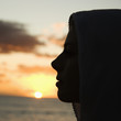 Photo: Woman with scarf over head against sunset over ocean. Woman with scarf over head against sunset over ocean.