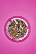 Full ashtray on pink background, view from above