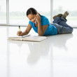 Asian preteen girl doing homework while talking on cell phone.