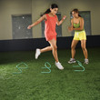 Girl jumping step hurdles while woman coach watches.