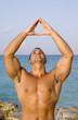 Young Man Meditating Near Ocean with Hand up in the Air