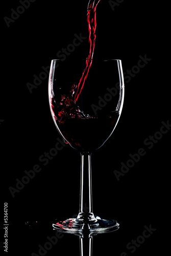 Red wine being poured into a glass splashing over the side.
