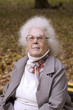 Old lady in the autumn park wearing glasses looking at you