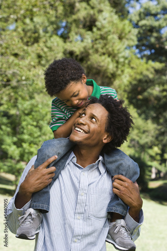 Photo: Father carrying son on shoulders in park. Father carrying son on shoulders in park.